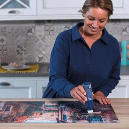 Woman in a kitchen setting, working on a puzzle with a tube of glue.