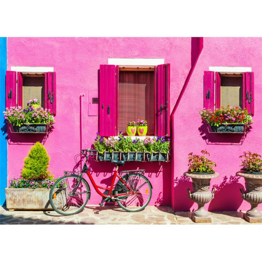 Red bicycle parked in front of a pink building with flower boxes. Burano Island Italy